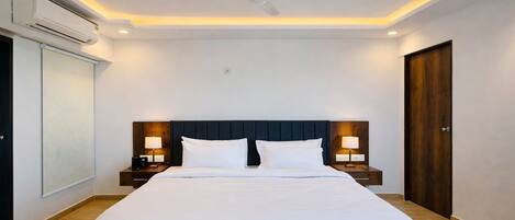 A hotel room with a large bed, two bedside tables with lamps, a ceiling fan, and an air conditioning unit.