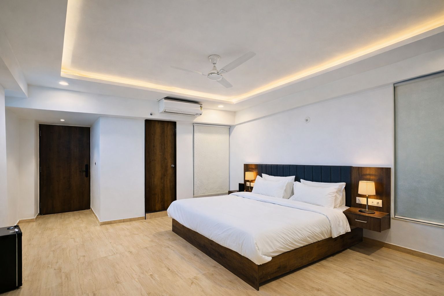 Habitación de hotel moderna con una cama grande, ventilador de techo, aire acondicionado, piso de madera y un ventanal amplio.