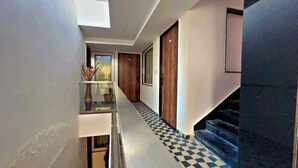 Un pasillo moderno con barandilla de vidrio, puertas de madera y un piso a cuadros que conduce a una escalera.