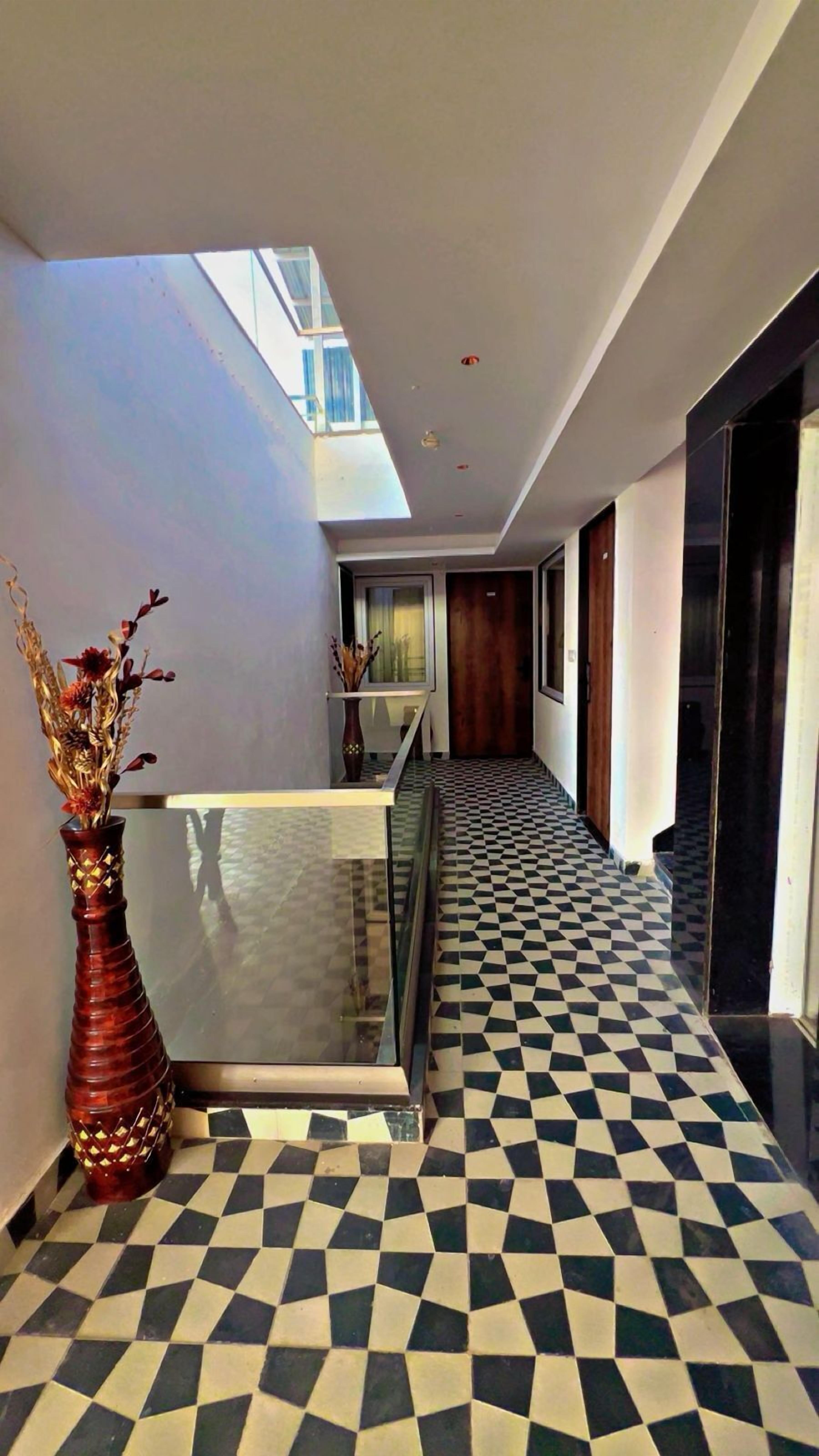 A hallway with a checkered floor, a glass railing, and a vase with dried flowers.