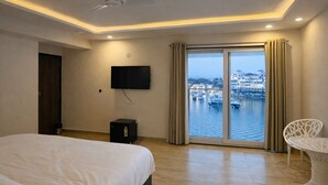 Habitación de hotel con una cama, un televisor montado en la pared, un altavoz pequeño y vista a un puerto con barcos y edificios.