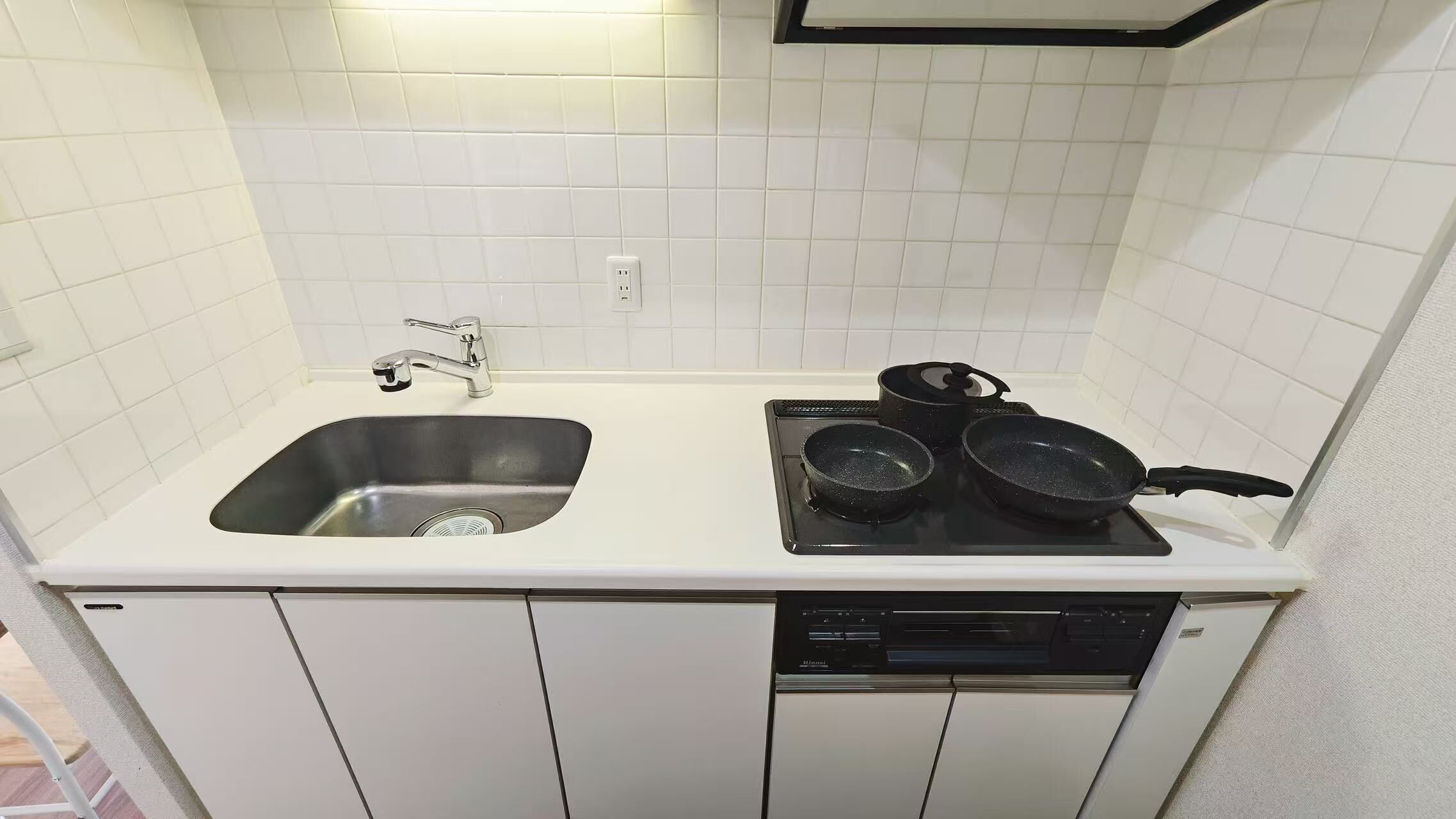 A compact kitchen with a stainless steel sink, a stove with two frying pans, and a dishwasher.