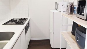 Eine kleine Küche mit weißen Schränken, einem Gasherd, einer Mikrowelle, einer Kaffeemaschine und einem Kühlschrank.