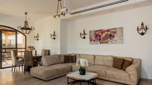 Un salón amplio con un sofá seccional beige grande, una mesa redonda de centro con un encaje y una araña.