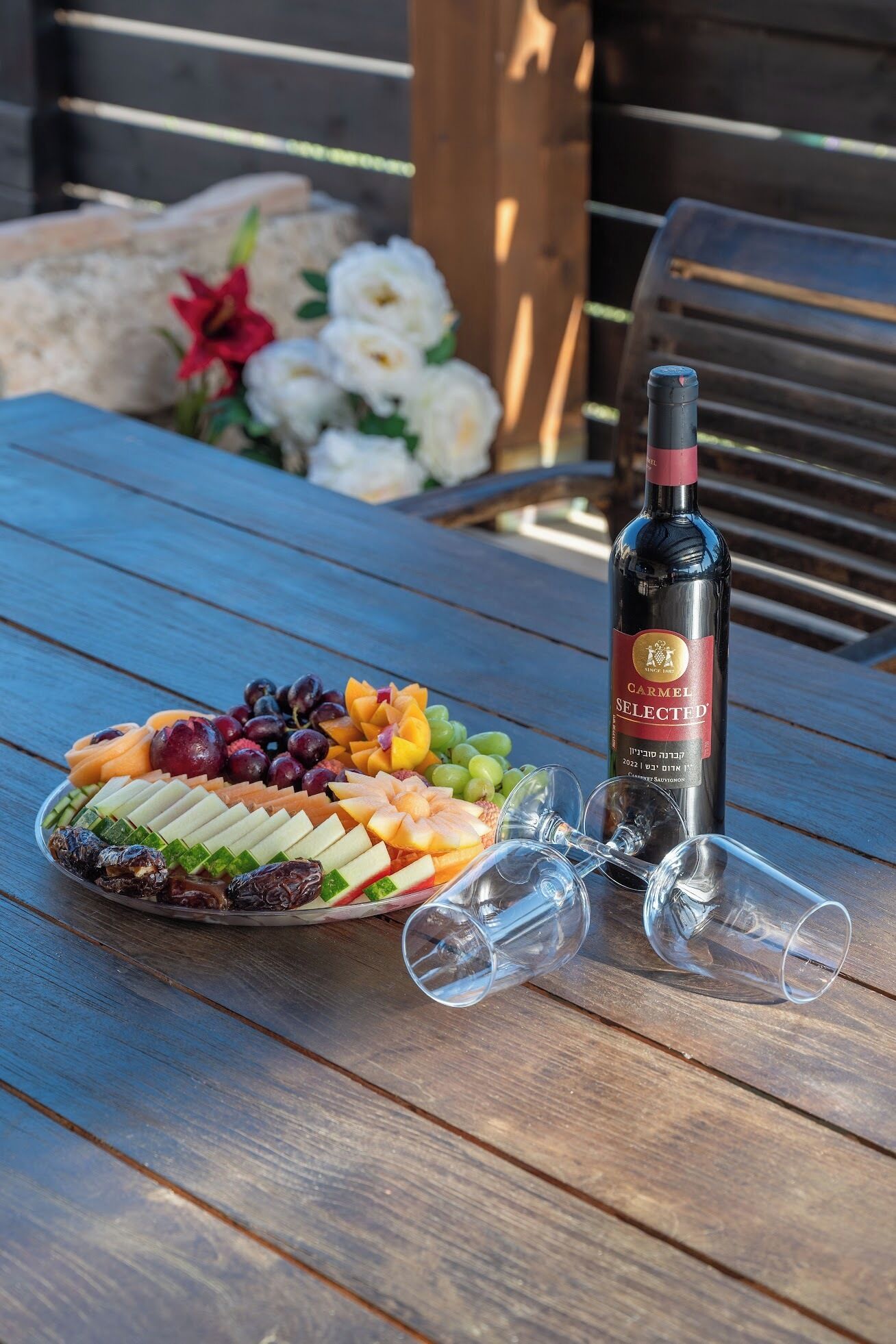 Une table en bois sur laquelle se trouvent un plateau de fruits, une bouteille de vin et deux verres à vin vides.