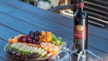 Une table en bois sur laquelle se trouvent un plateau de fruits, une bouteille de vin et deux verres à vin vides.