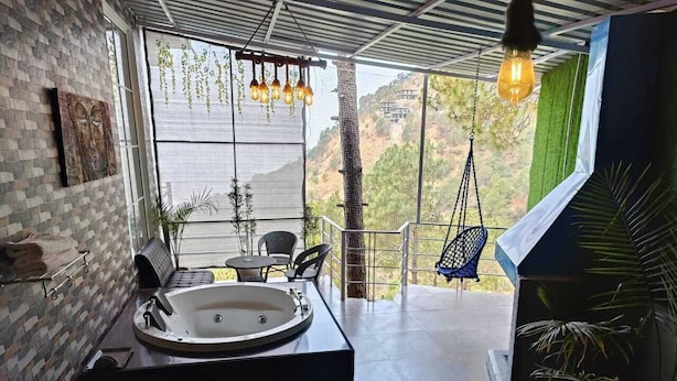 A modern bathroom with a large bathtub, a hanging light fixture, and a view of a mountainous landscape. - The Pine Paradise (Kasauli)