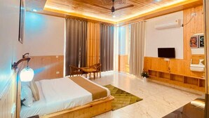 A modern hotel room with a wooden ceiling, a bed, a desk, a TV, and a bathroom. - The Pine Paradise (Kasauli)