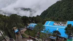 A resort with a blue-roofed building surrounded by lush greenery and a mountainous backdrop. - The Pine Paradise (Kasauli)
