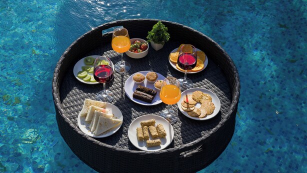 Mesa flutuante com diversos alimentos e bebidas sobre uma piscina.