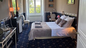 A bedroom with a bed, bedside table, lamp, chair, and a window with a view of greenery. - Gite in manor near futuroscope (Saint-Martin-la-Pallu)