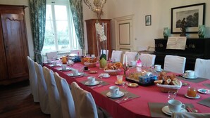 A dining room with a long table set for breakfast, featuring bread, pastries, and fruit. - Gite in manor near futuroscope (Saint-Martin-la-Pallu)