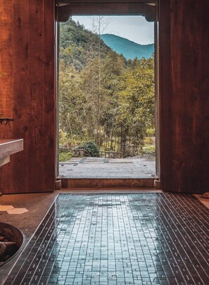 Interior de madera con piso de baldosas que conduce a una vista de un paisaje montañoso.