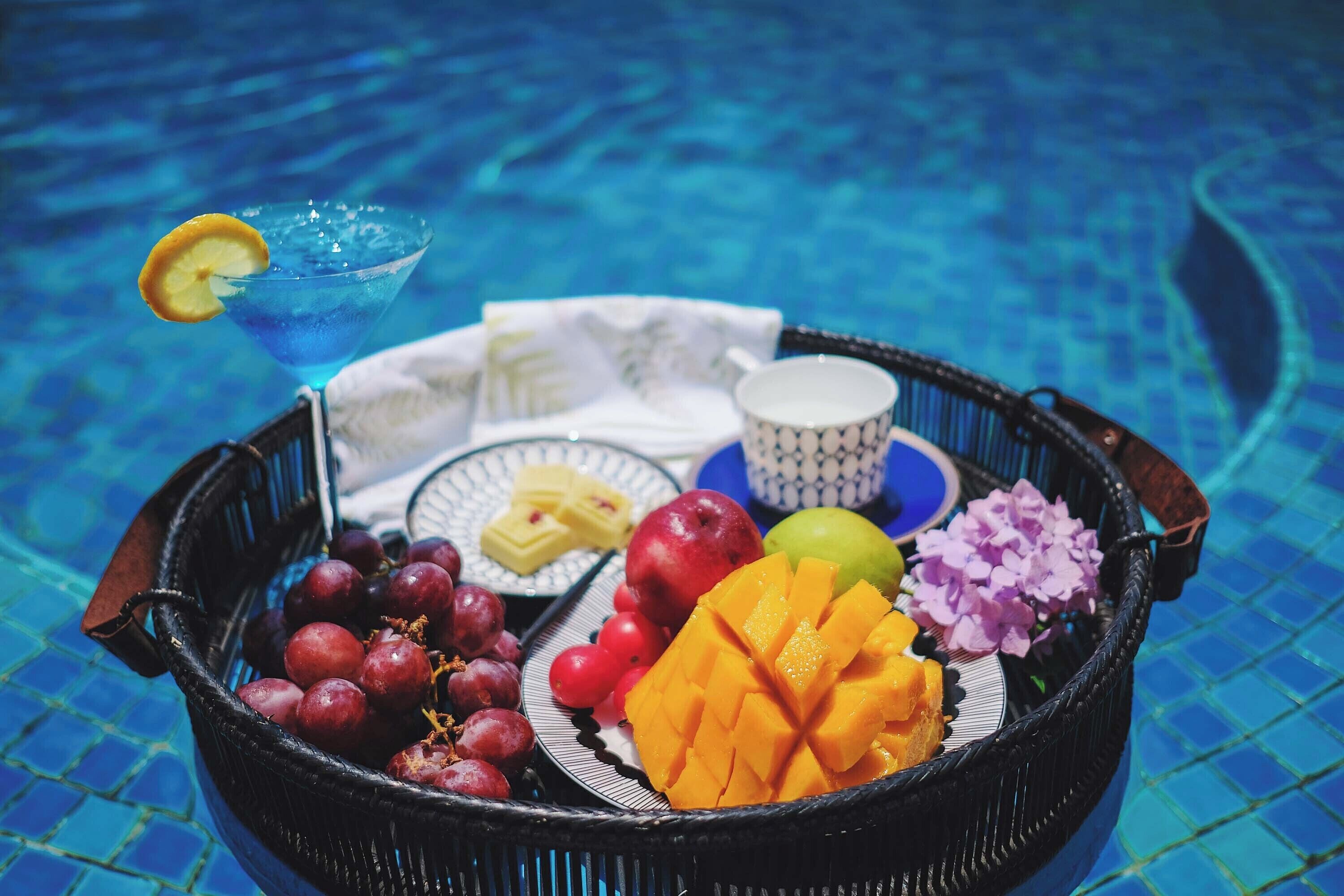 A fruit basket with grapes, mango, apple, and flowers on a tiled surface.