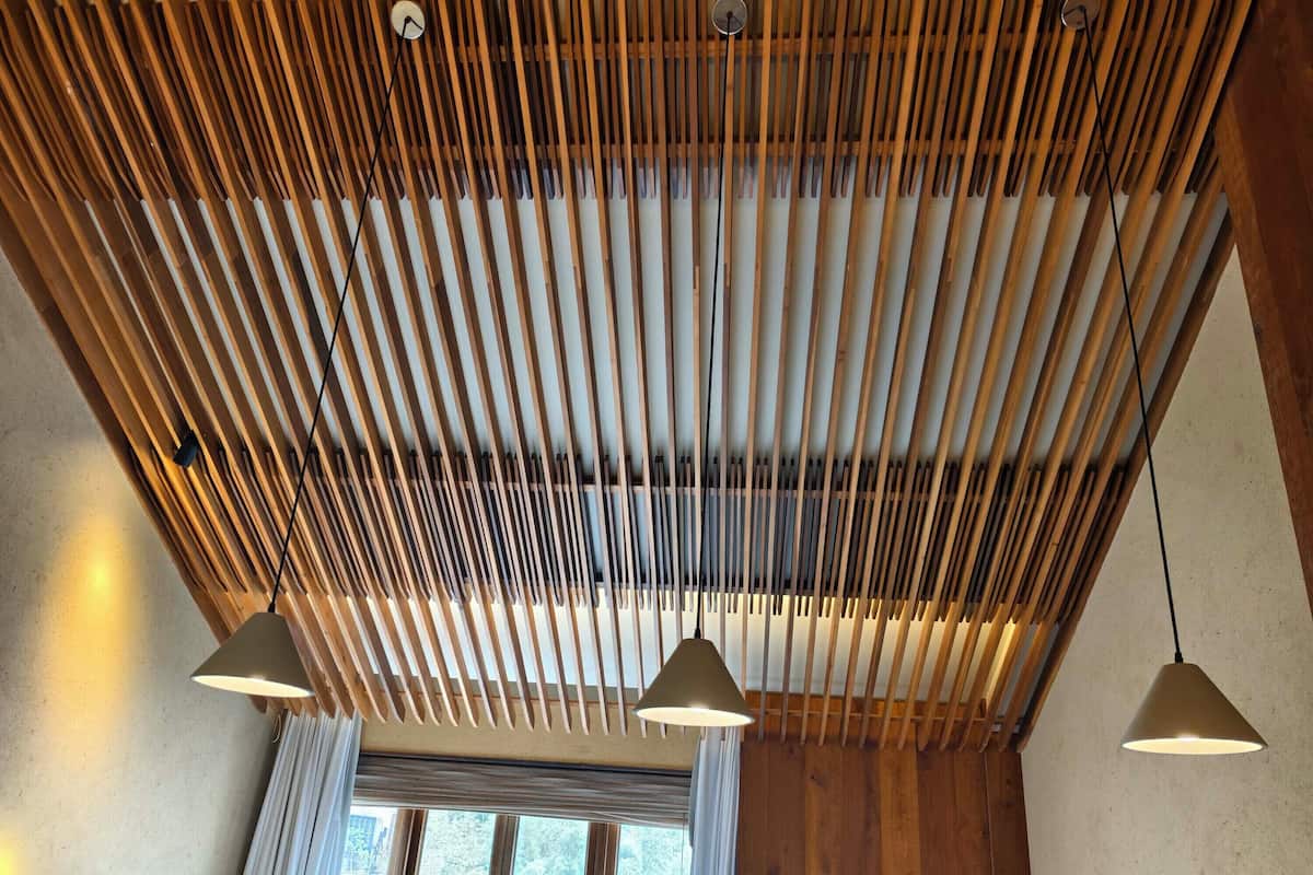 A room with a slatted wooden ceiling, a large window with blinds, and pendant lighting.