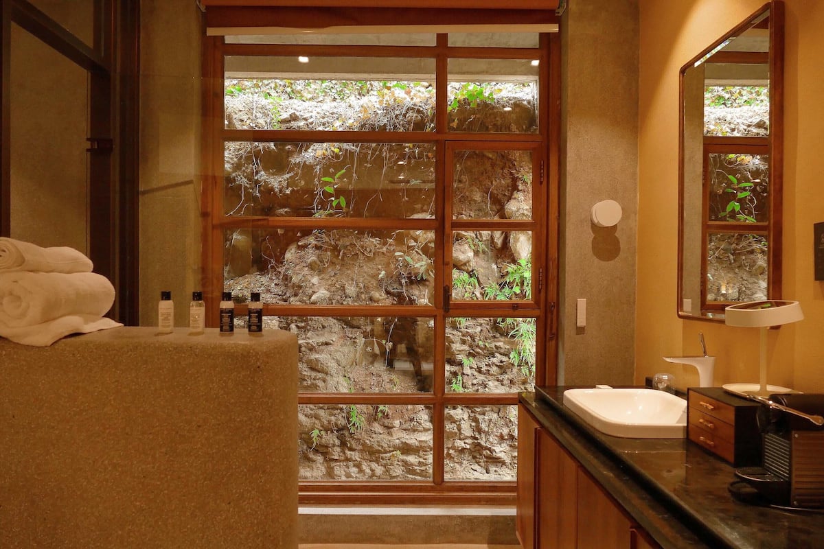 A bathroom with a large window, a sink, and toiletries on the counter.