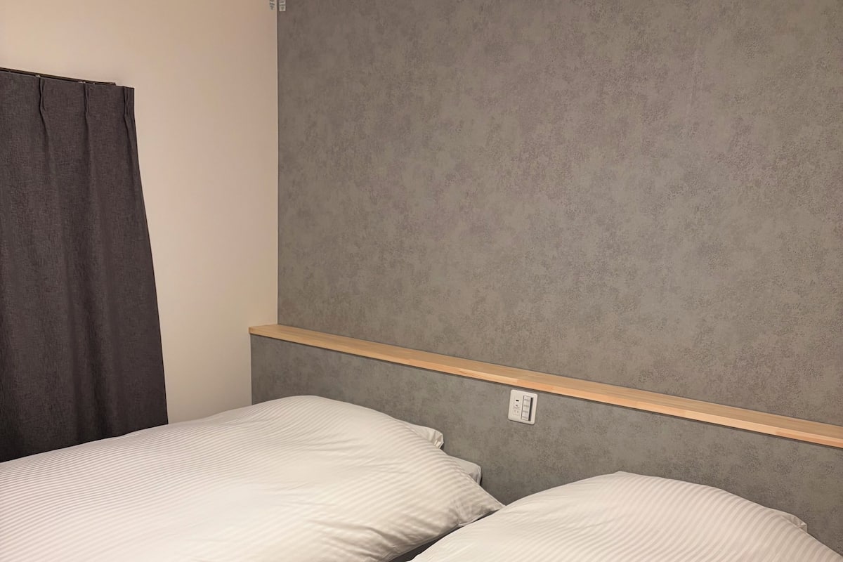 A bedroom with two beds, a grey headboard, and a wooden shelf above the beds.