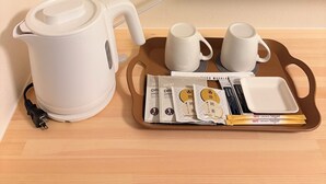 A white electric kettle, two white cups, a tray with tea packets, and a small white plate on a wooden table against a beige wall. - HOTEL LUNA STELLA (Sendai)
