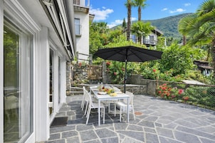 A patio with a stone table and chairs, surrounded by lush greenery and a mountain backdrop.