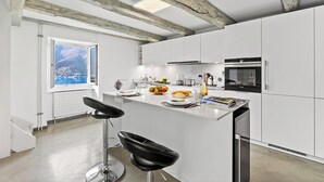 Eine moderne Küche mit weißen Schränken, einer zentralen Kücheninsel und einem großen Fenster mit Blick auf eine gebirgige Landschaft.