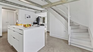 Eine geräumige Küche mit einer zentralen Kochinsel, weißen Schränken und einer Treppe zu einer oberen Ebene.