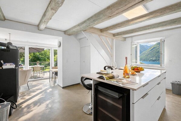 Uma cozinha moderna com uma ilha grande, uma área de refeições com cadeiras e vista para montanhas através de uma janela.