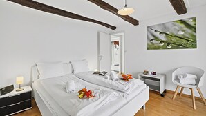 A modern bedroom with a large bed, a bedside table with a lamp, a chair, and a wall-mounted picture. - Casa la Tortue 2 Scaiano for 6 (Gambarogno)