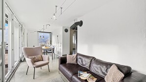 A modern living room with a leather sofa, a plush armchair, and a dining area in the background. - Casa la Tortue 2 Scaiano for 6 (Gambarogno)