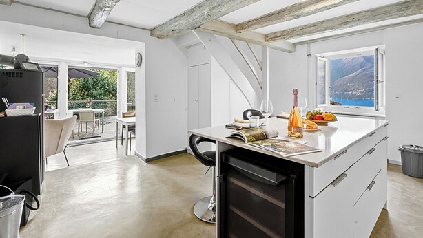 A modern kitchen with a large island, a dining area with chairs, and a view of the outdoors. - Casa la Tortue 2 Scaiano for 6 (Gambarogno)