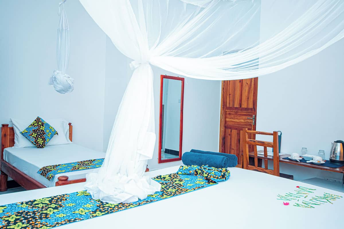 A room with two beds, a wooden chair, a table with a kettle, and a mirror.