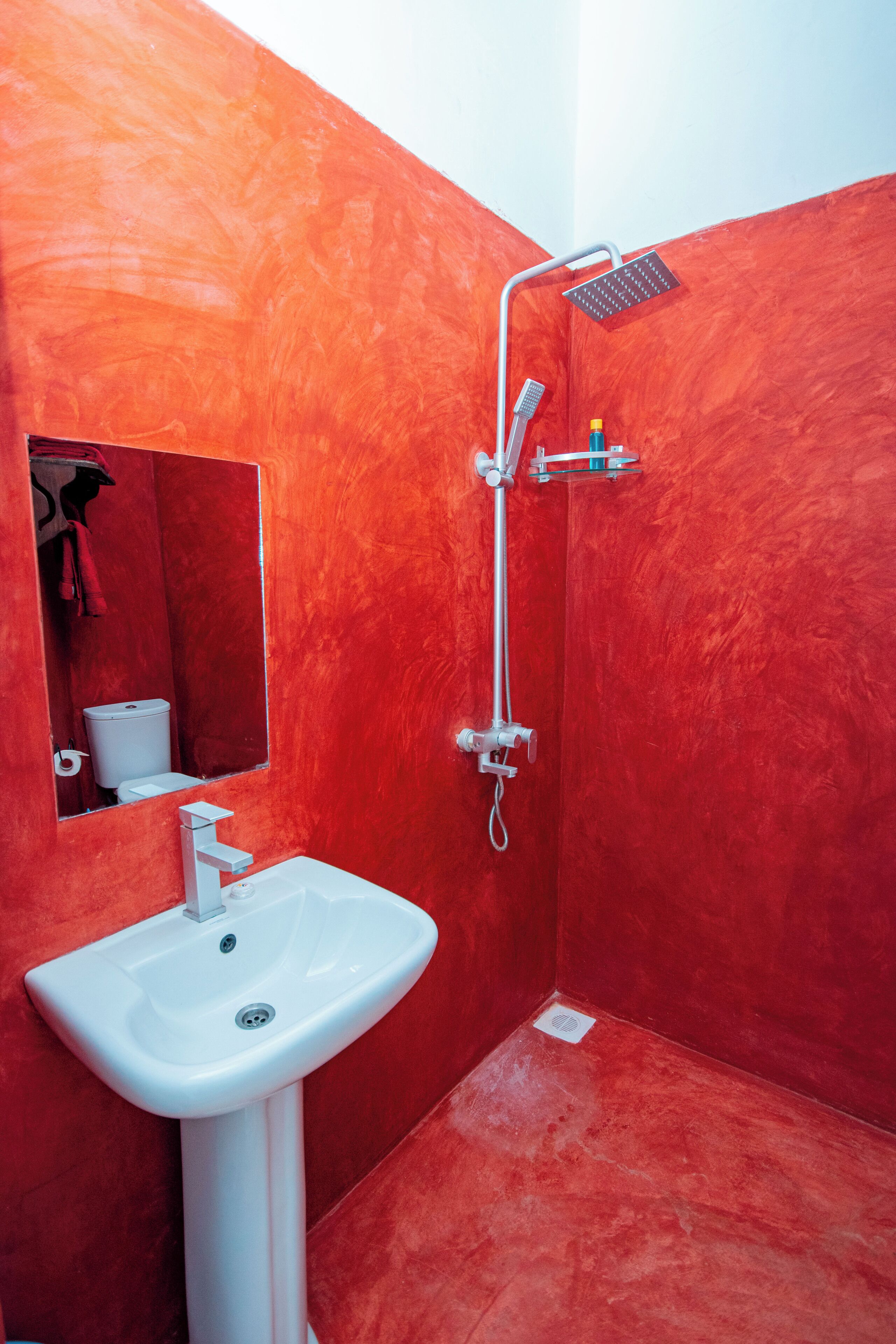 A bathroom with a red wall, a white sink, and a shower.