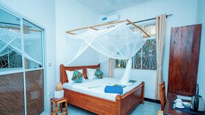 Ein hölzernes Bett mit Baldachin, ein kleiner Nachttisch, ein Stuhl, ein Schreibtisch mit Wasserkocher und ein Fenster mit schmiedeeisernen Verzierungen.