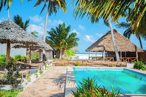 A pool area with thatched-roof structures, palm trees, and a clear blue sky. - Pongwe Beachfront Villa (Pongwe)