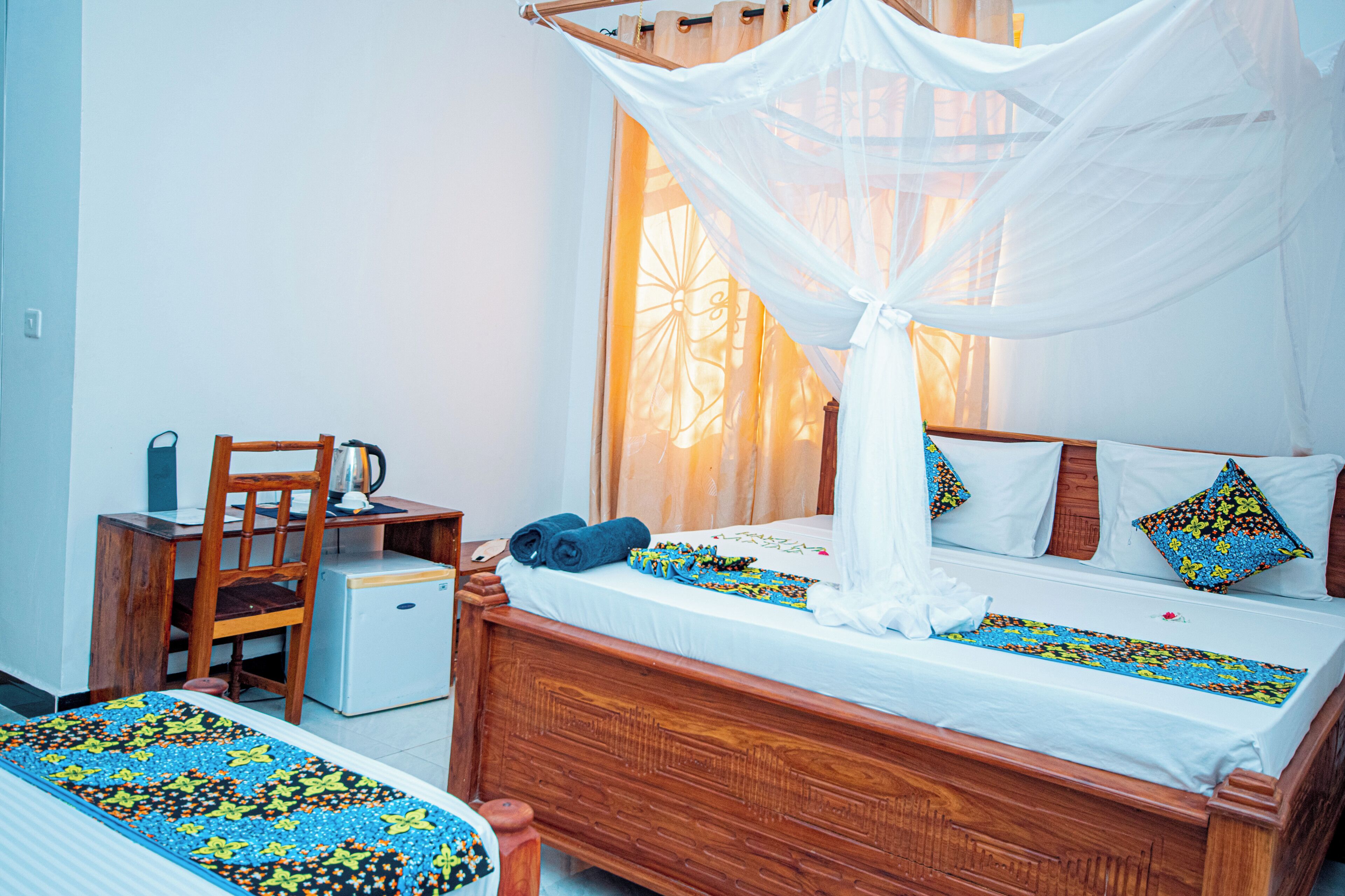 A bedroom with a wooden bed, a chair, a desk, and a small refrigerator.