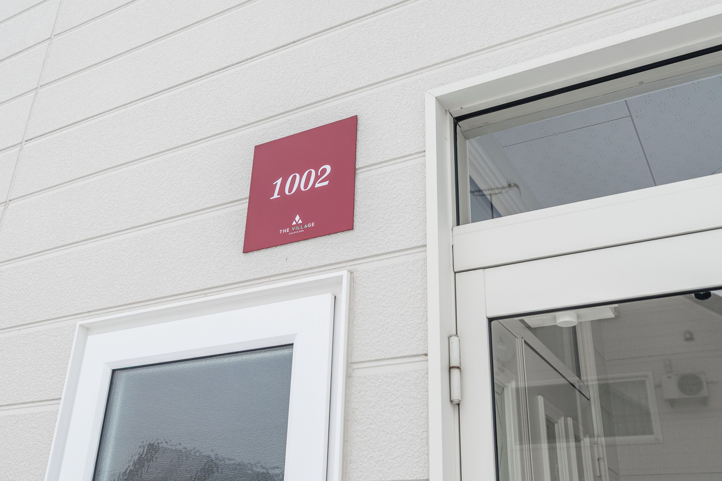 Un edificio con fachada blanca y un cartel rojo que muestra el número 1002.
