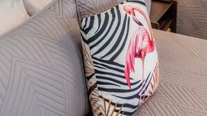 A bed with a headboard, a pillow with a flamingo design, and a bedside lamp. - Flamingo Inn - 2 Queen with Kitchenette #204 (Fort Myers Beach)