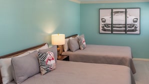 A hotel room with two beds, a nightstand with a lamp, and a wall-mounted picture of a car. - Flamingo Inn - 2 Queen with Kitchenette #204 (Fort Myers Beach)
