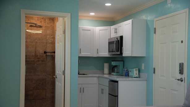 A bedroom with a bed, a shower, a microwave, and a coffee maker. - Flamingo Inn - 2 Queen with Kitchenette #204 (Fort Myers Beach)