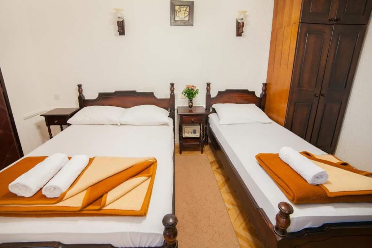 A hotel room with two beds, each with a wooden headboard, white linens, and towels. There is a small table with a vase of flowers between the beds.