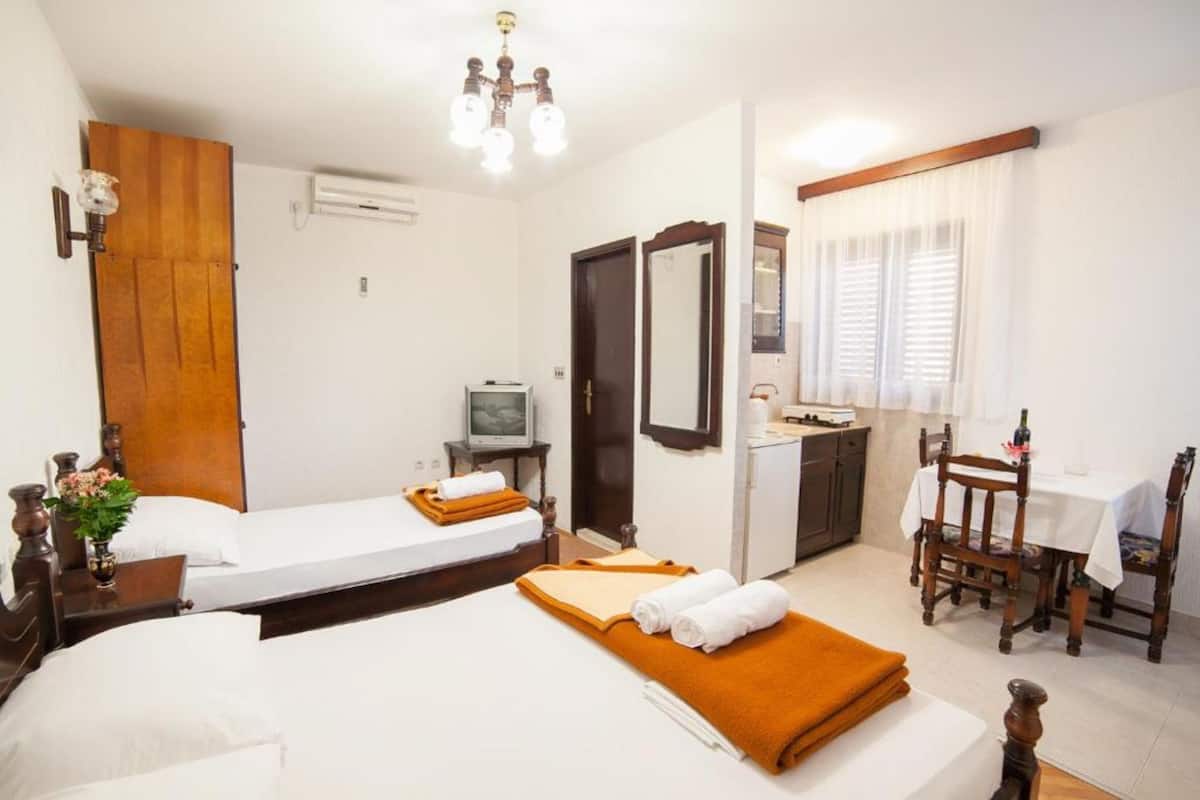 A hotel room with two beds, a small kitchenette, a dining table with chairs, a mirror, and a television.