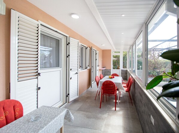 A corridor with a table and chairs, a window with a view, and a door with shutters. - Guest House 4M Gregović (Petrovac)