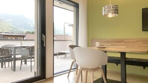 A modern room with a sliding glass door leading to a balcony, a wooden table, a white chair, and a hanging pendant light. - Apartment Luis 3 - Alpstay (Naturns)