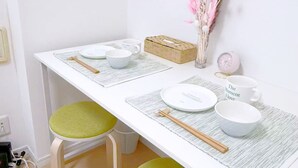 Une table à manger blanche, des chaises vertes avec des coussins, un set de table en fibres tressées et un petit vase contenant des fleurs séchées.