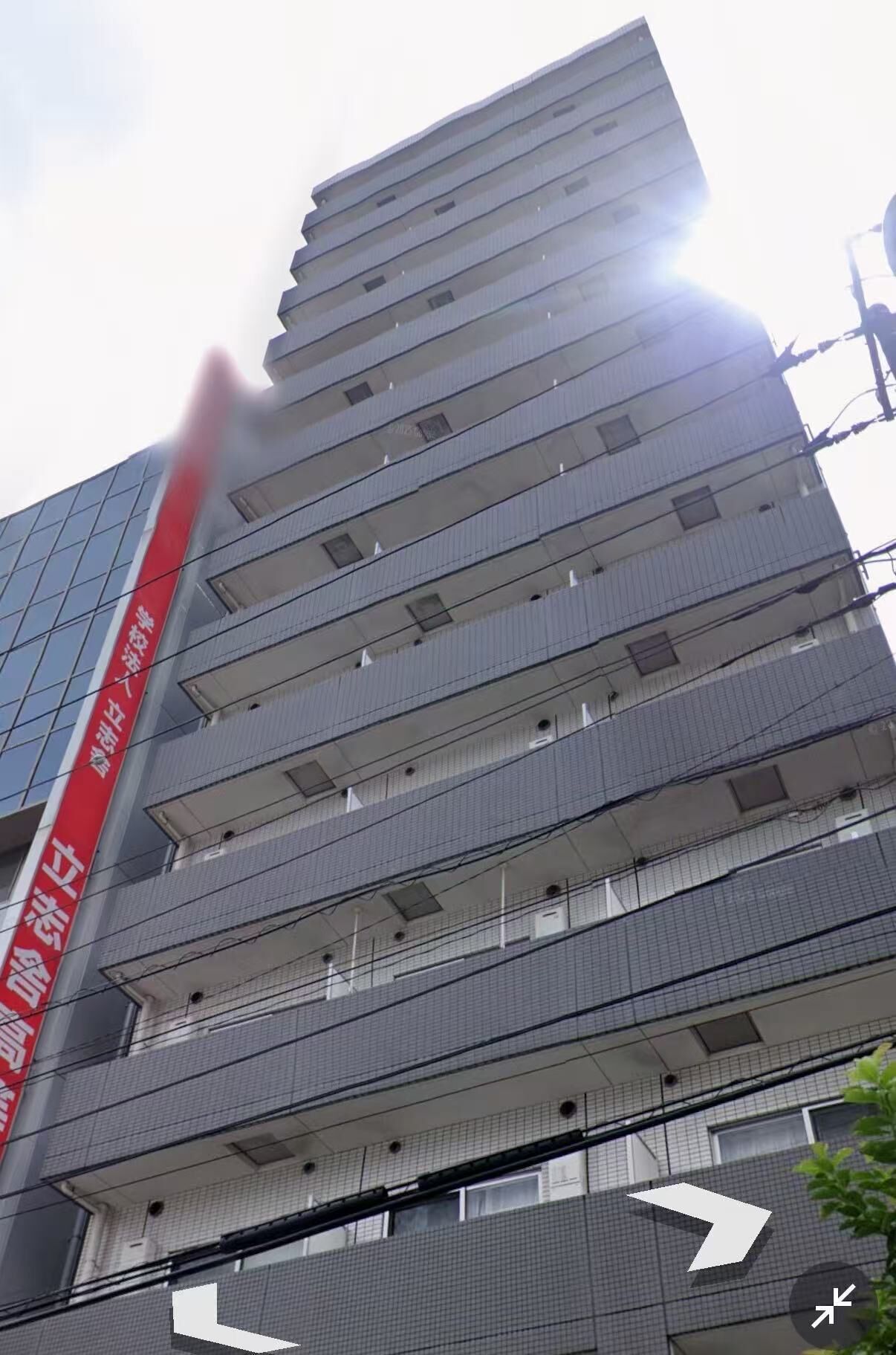 Un immeuble à plusieurs étages, doté d’une enseigne verticale rouge, de nombreux balcons et d’une façade à motifs géométriques.