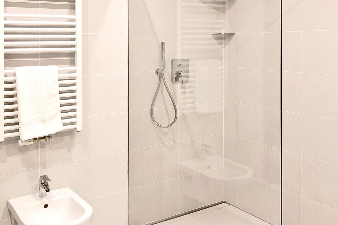 Une salle de bain moderne avec une douche à parois de verre, un lavabo blanc et un porte-serviettes.