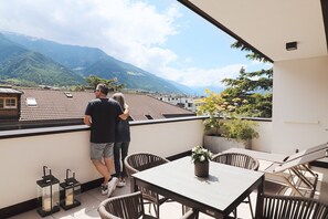Un balcon avec une table et des chaises, un pot de fleurs et une vue sur les montagnes.