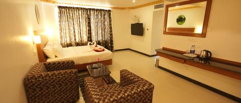 A hotel room with a bed, two patterned armchairs, a small table, a TV, a mirror, and a coffee maker.