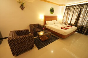 A hotel room with a bed, two patterned armchairs, a small table, and a decorative wall piece.