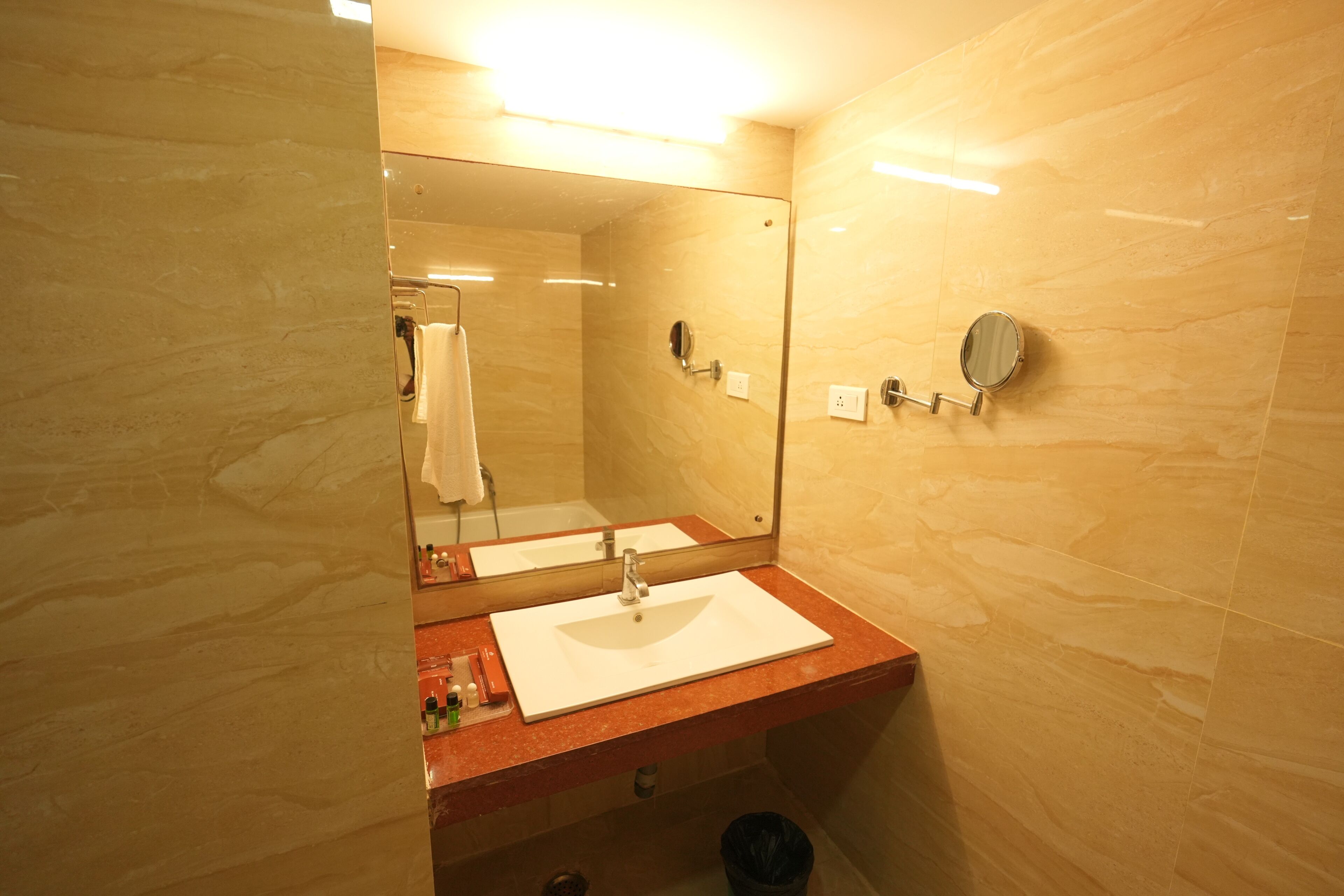 A bathroom with a marble wall, a sink with a mirror, and a towel hanging on the wall.