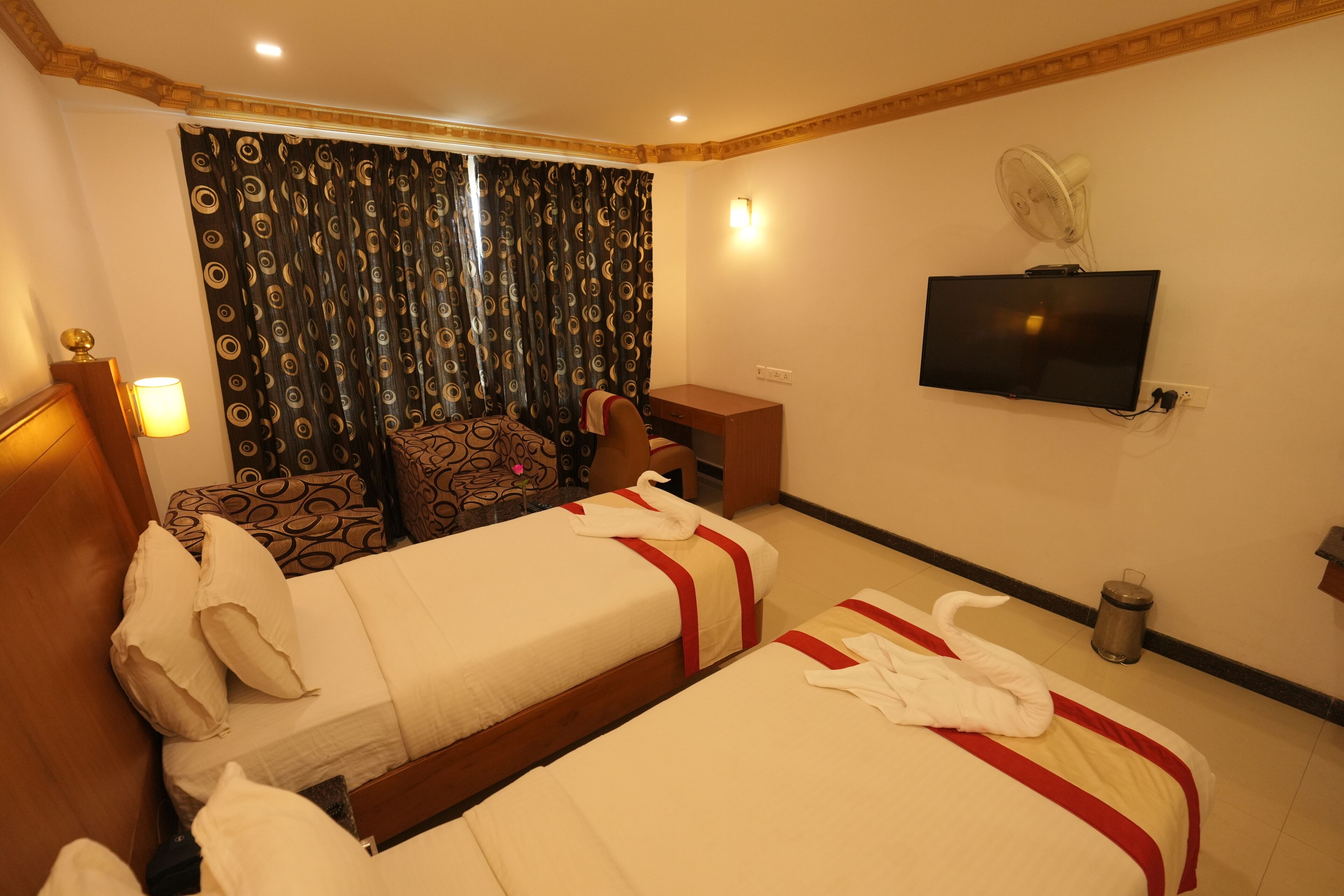 A hotel room with two beds, a desk, a TV, and a curtain with a circular pattern.